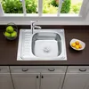 A stainless steel kitchen sink with a faucet, a basket of green apples, and a bowl of oranges on a dark countertop, with a window showing greenery in the background. Náhľad obrázku produktu