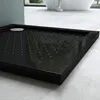 A close-up, angled view of a black shower tray with a drain cover and textured surface, placed on a light gray tiled floor. Produktbild-Vorschau
