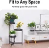A black metal plant stand with three tiers, holding various potted plants, is placed next to a white media console with decorative items. Náhľad obrázku produktu