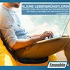 A person is sitting on a yellow cushion with a laptop on their lap, using a black seat cushion. Produktbild-Vorschau