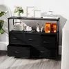 A black storage cabinet with multiple drawers and shelves, placed in a room setting with a plant and couch visible. Anteprima dell’immagine prodotto