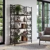 A black metal bookshelf with decorative cutouts is placed in a room with large windows and a chair. Náhled obrázku produktu