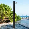 An outdoor shower on a beach next to lush green bushes and the ocean. Produktbild-Vorschau
