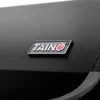 A close-up shot of a black grill with a silver and red TAINO logo. Produktbild-Vorschau