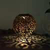 A decorative spherical lantern with a cut-out pattern is lit from within, casting intricate shadows on a dark surface. Produktbild-Vorschau
