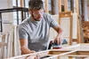 A man is sanding a wooden frame in a workshop. Anteprima dell’immagine prodotto