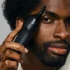 A man is holding a black grooming device to his face. Produktbild-Vorschau