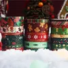 Stacks of Christmas-themed washi tape rolls arranged in artificial snow with a blurred Christmas tree and gingerbread house in the background. Produktbild-Vorschau