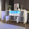 A modern white sideboard with gold accents and LED lighting, displayed in a room with dark wood paneling and a patterned rug. Produktbild-Vorschau
