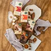 A collection of Naturata cocoa and powdered sugar products arranged on a wooden surface, with some cookies and cocoa powder scattered around. Anteprima dell’immagine prodotto