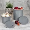 Two ceramic storage jars for onions and garlic, with a potted herb and some loose onions in the foreground. Produktbild-Vorschau
