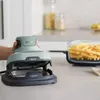 A hand is holding a green and gray Ninja CRISPi air fryer, with a glass dish full of french fries next to it on a kitchen counter. Anteprima dell’immagine prodotto