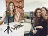 A collage of two lifestyle shots. The left shows a woman applying makeup while holding a makeup brush, with a tripod and phone holder on the table. The right shows two women taking a selfie outdoors. Produktbild-Vorschau