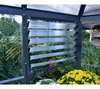 A greenhouse with louvre windows and yellow flowers in the foreground. Produktbild-Vorschau