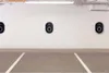 Three black wall-mounted electric vehicle charging stations are mounted on a white wall in a parking garage. The floor is concrete with white parking lines. Produktbild-Vorschau