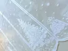A close-up view of a white lace curtain with a Christmas tree and gift pattern. Produktbild-Vorschau