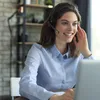 A woman wearing a headset is smiling and looking at a laptop screen, suggesting she is on a call or in a meeting. Produktbild-Vorschau