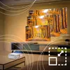 A projector is shown on a table in a living room, projecting images of a forest onto a wall. Different screen sizes are indicated on the projected image. Voir les images du produit