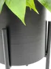 A close-up view of a black metal plant stand with a textured surface, holding a green plant. Produktbild-Vorschau