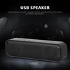 A black USB speaker is shown on a dark, reflective surface with a blurred background. Produktbild-Vorschau