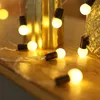 A close-up shot of a string of fairy lights with small, round, white bulbs and black connectors, resting on a wooden surface. Náhled obrázku produktu