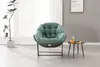 A green papasan chair with a small side table next to it, in a room with a window and a framed picture on the wall.