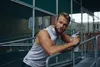 A man is leaning on a railing outdoors, holding a shaker bottle. Produktbild-Vorschau