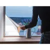 A person is applying a silver window film to a window. There is a vase with lavender flowers on the windowsill. Produktbild-Vorschau