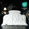 A white duvet and pillows are displayed on a bed against a dark, floral wallpaper background. A bedside table with a lamp and a framed picture is visible to the left. A logo and text are in the upper right corner. Produktbild-Vorschau