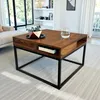 A square wooden coffee table with a black metal frame is shown in a living room setting. Produktbild-Vorschau