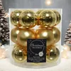A clear plastic container filled with gold Christmas baubles, set against a festive, snowy background with blurred Christmas trees. Produktbild-Vorschau