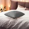 A gray quilted pillow rests on a bed with Christmas lights and trees in the background. Podgląd zdjęcia produktu