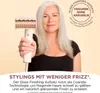 A woman with grey hair is holding a hair dryer attachment. Voir les images du produit