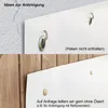 Two images showing different ways to hang a white poster. The top image shows the poster with metal eyelets attached to a textured wall, with hooks visible. The bottom image shows the poster with small wooden pegs attached to a wooden wall, suggesting atta Produktbild-Vorschau