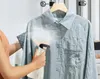 A person is using a handheld steamer to remove wrinkles from a light blue shirt hanging on a hanger. Produktbild-Vorschau