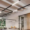 Modern office interior with suspended linear LED lights, a green wall, and modular seating. Voir les images du produit