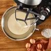 A close-up overhead view of a kitchen mixer with a batter in its bowl, placed on a wooden surface with baking ingredients like eggs and flour nearby. Produktbild-Vorschau