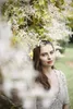 A woman is posing outdoors, partially obscured by white flowers, wearing a decorative dress. Náhľad obrázku produktu