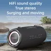 A portable speaker is placed on rocks near the water, with text overlays describing its features. Produktbild-Vorschau