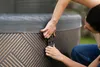 Two people are shown securing the cover of an inflatable hot tub outdoors. Náhled obrázku produktu