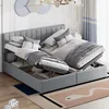 A bedroom scene with a grey upholstered bed frame, featuring two open storage compartments revealing bedding and storage items. The bed is made with white and grey linens and pillows. A decorative wall art and curtains are visible in the background. Produktbild-Vorschau