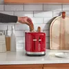 A hand placing a slice of bread into a red toaster on a kitchen counter. Anteprima dell’immagine prodotto