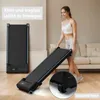 A woman is holding a compact treadmill in a living room setting. Produktbild-Vorschau