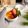 A hand holding a crème brûlée in a ramekin, garnished with a strawberry and mint leaves. Voir les images du produit