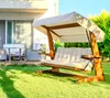A wooden swing set with beige cushions is set up on a green lawn in front of a modern house. Produktbild-Vorschau
