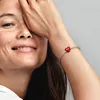 A woman's arm wearing a bracelet with a red heart charm. Produktbild-Vorschau