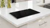 A black glass stovetop cover rests on a white speckled countertop in a modern kitchen. Podgląd zdjęcia produktu