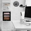 A mini fridge stocked with drinks is placed next to a desk with a computer monitor, keyboard, mouse, and a mug. A clock and a decorative cactus are on the shelf above the fridge. Voir les images du produit