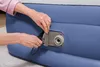 A close-up shot of a person's hands interacting with the inflation valve of a blue air mattress. Produktbild-Vorschau