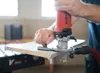 A person is using a red and silver Mafell edge router on a piece of wood, which is placed on a black workbench with red lettering. Produktbild-Vorschau
